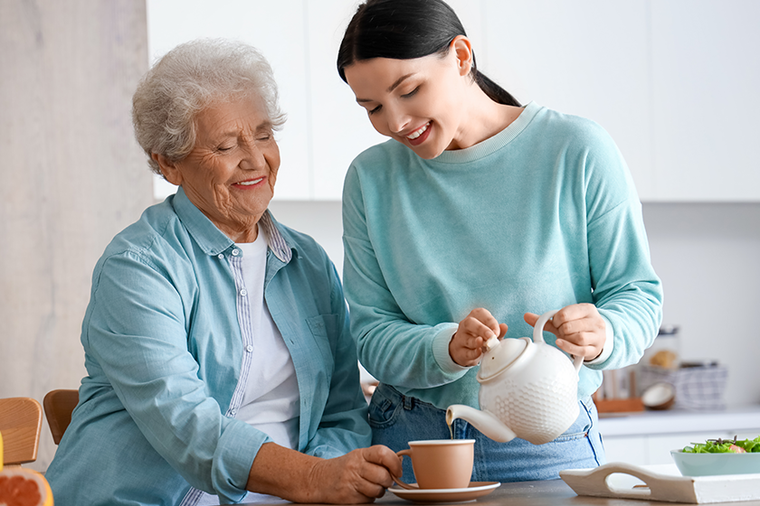 Young woman pouring hot tea for her mother in kitchen 